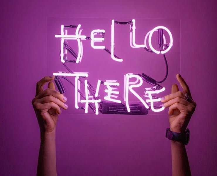 Zwei Hände halten ein Neonlicht Schild mit den Worten "Hello there"